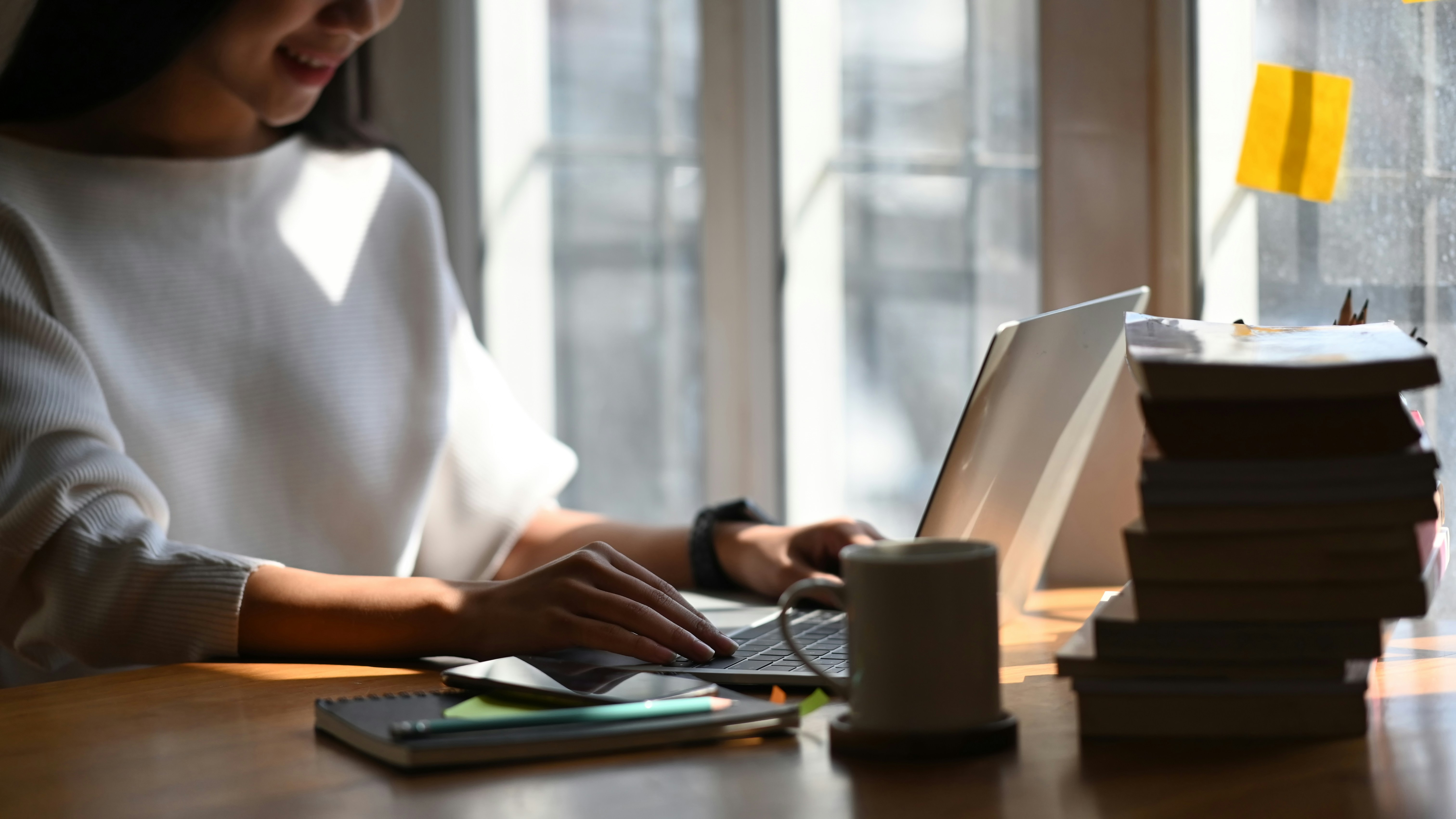 Person writing on a laptop beside books and notes, illustrating the creation of original content and intellectual property.